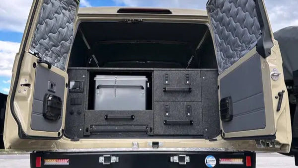 Back of a beige off-road vehicle with open cargo doors on a cloudy day showcasing a premium drawer system